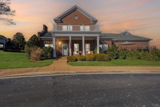 view of front of house featuring a balcony, covered porch, and a lawn