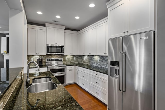 kitchen with stainless steel appliances, white cabinetry, sink, and dark stone counters