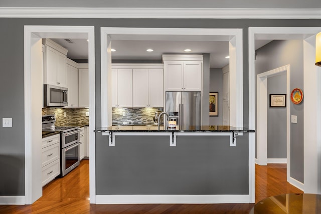 kitchen featuring dark stone countertops, a breakfast bar area, white cabinets, decorative backsplash, and stainless steel appliances