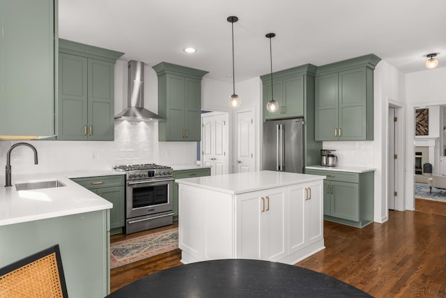 kitchen with appliances with stainless steel finishes, wall chimney range hood, decorative light fixtures, sink, and dark wood-type flooring