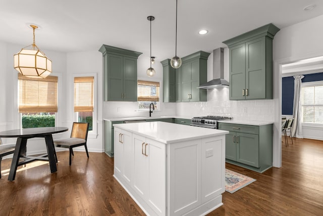 kitchen with high end stainless steel range, hanging light fixtures, green cabinets, and wall chimney exhaust hood