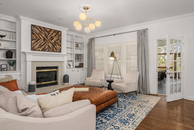 living room featuring crown molding, built in shelves, a fireplace, dark hardwood / wood-style floors, and a notable chandelier