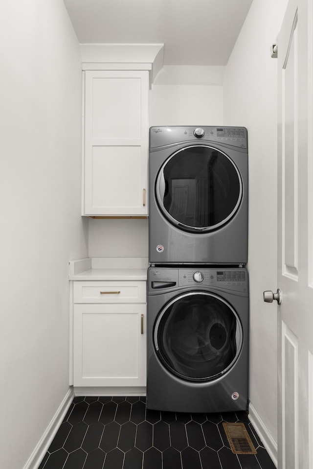 laundry area featuring dark tile patterned flooring, cabinets, and stacked washing maching and dryer