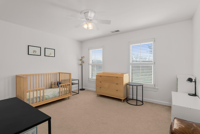 carpeted bedroom with a crib and ceiling fan