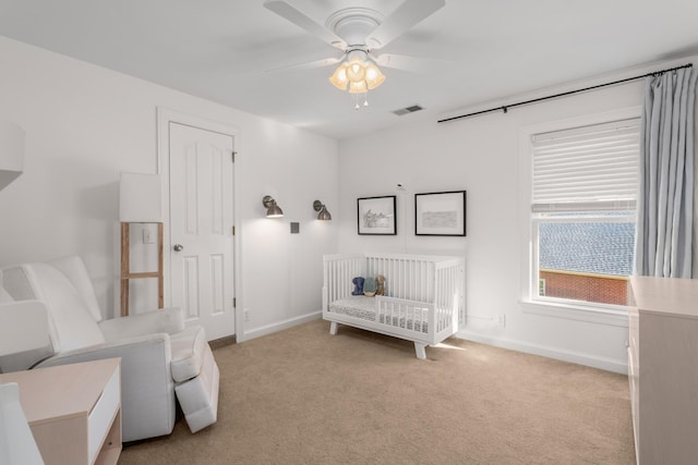 bedroom featuring light carpet, a crib, and ceiling fan