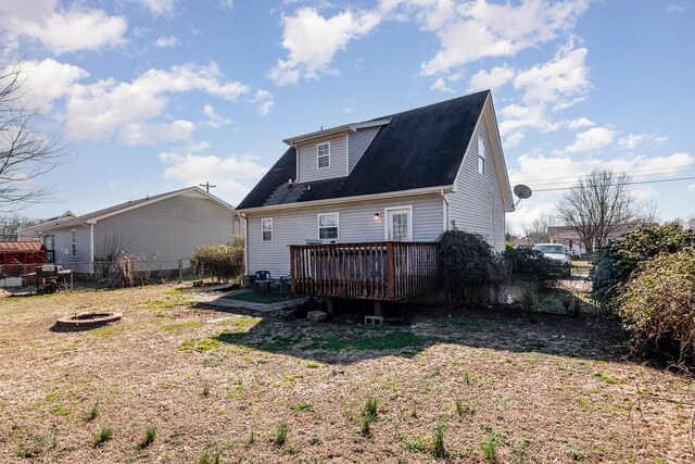 rear view of property featuring a wooden deck, a lawn, and a fire pit