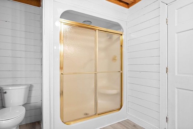 bathroom with wood-type flooring, toilet, a shower with shower door, and wood walls