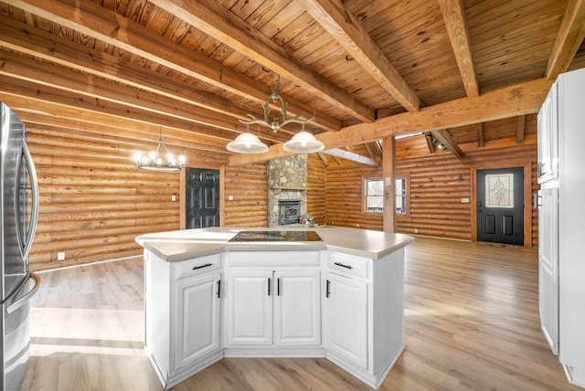 kitchen with pendant lighting, log walls, stainless steel fridge, and white cabinets