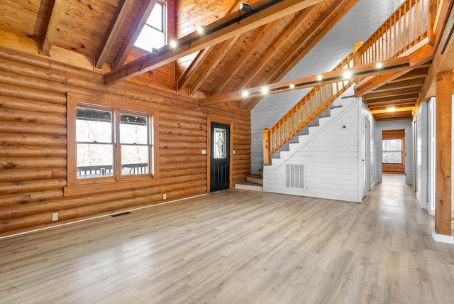 unfurnished living room featuring a healthy amount of sunlight, light wood-type flooring, log walls, and high vaulted ceiling