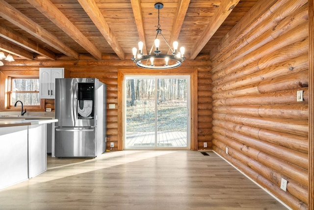 kitchen with stainless steel refrigerator, beamed ceiling, white cabinets, rustic walls, and hanging light fixtures