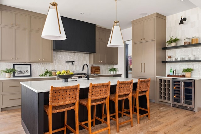 kitchen featuring a center island with sink, wine cooler, tasteful backsplash, and light wood-type flooring