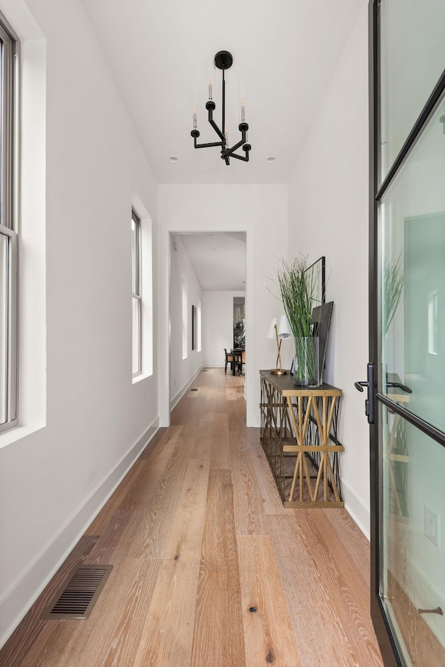 corridor with a notable chandelier, light wood-style floors, visible vents, and baseboards