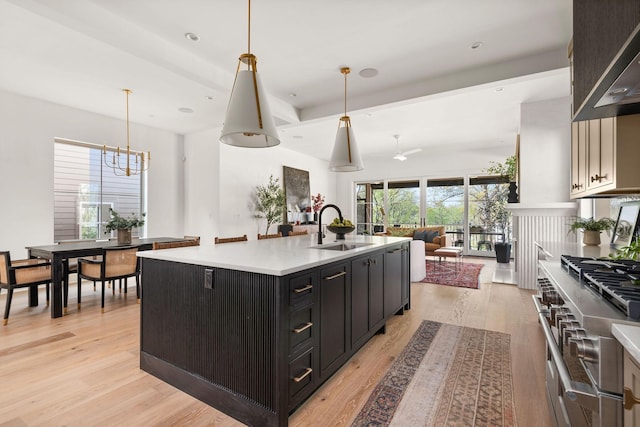 kitchen with a sink, stainless steel range with gas stovetop, open floor plan, light wood-style flooring, and dark cabinets