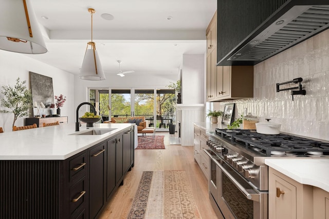 kitchen featuring light wood finished floors, a sink, tasteful backsplash, wall chimney range hood, and range with two ovens