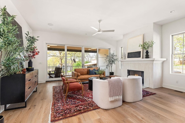 living area featuring wood finished floors, baseboards, visible vents, ceiling fan, and a lit fireplace