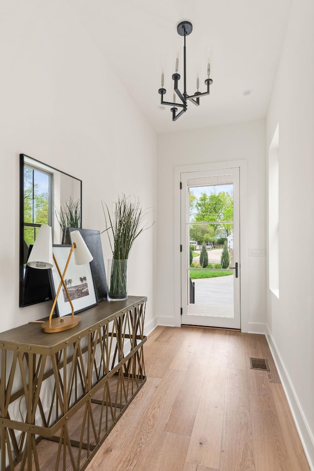 doorway to outside with light wood finished floors, visible vents, baseboards, and a notable chandelier