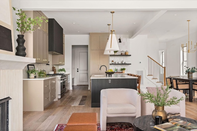 kitchen featuring light wood-type flooring, high end stainless steel range oven, wall chimney exhaust hood, light countertops, and decorative backsplash