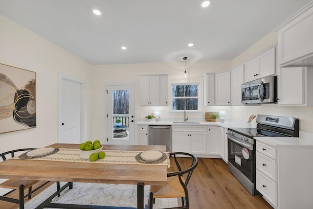 kitchen featuring sink, hardwood / wood-style flooring, white cabinetry, stainless steel appliances, and decorative light fixtures