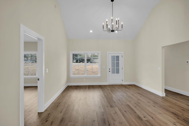 unfurnished dining area featuring light wood-type flooring, high vaulted ceiling, and an inviting chandelier