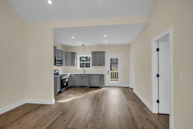 kitchen featuring appliances with stainless steel finishes, gray cabinetry, sink, light wood-type flooring, and pendant lighting