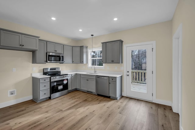 kitchen with appliances with stainless steel finishes, sink, hanging light fixtures, gray cabinets, and light hardwood / wood-style flooring