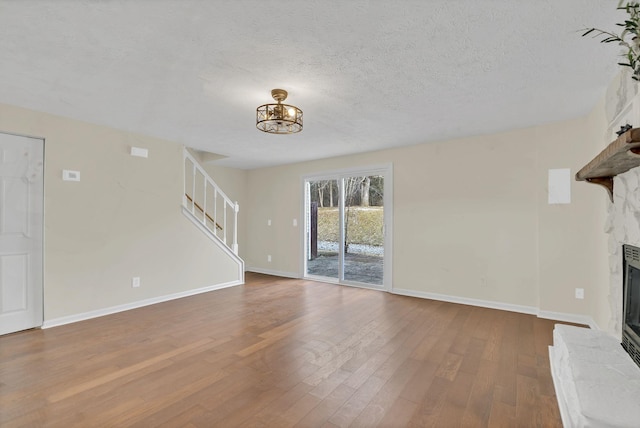 unfurnished living room featuring hardwood / wood-style floors, a textured ceiling, a notable chandelier, and a fireplace