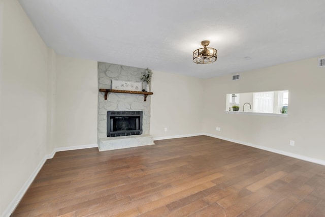 unfurnished living room with hardwood / wood-style flooring, heating unit, and a stone fireplace