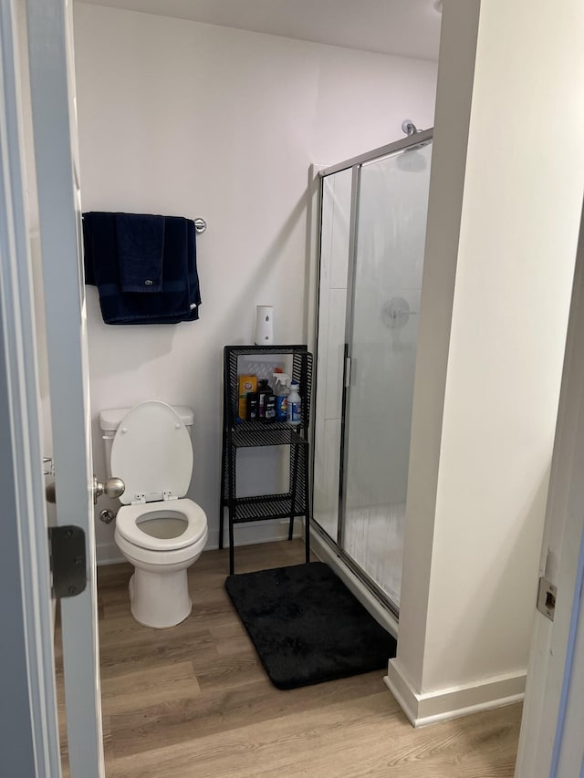 bathroom with wood-type flooring, a shower with door, and toilet