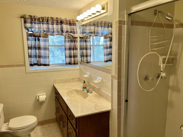 bathroom featuring a textured ceiling, a shower with door, vanity, tile walls, and toilet