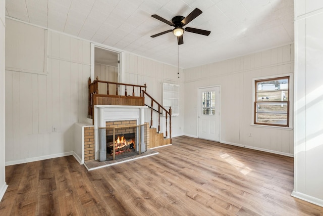 unfurnished living room with ceiling fan, wood-type flooring, wooden walls, and a brick fireplace