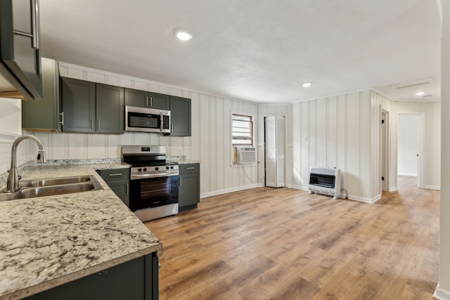 kitchen with heating unit, sink, light stone counters, light hardwood / wood-style floors, and stainless steel appliances