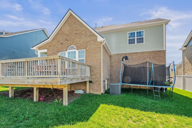 back of property with a trampoline, central AC unit, a wooden deck, and a yard