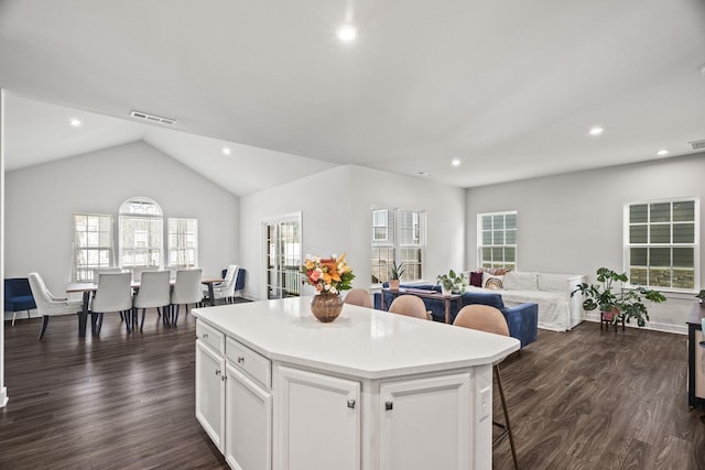 kitchen with a center island, dark wood-type flooring, white cabinetry, vaulted ceiling, and a breakfast bar