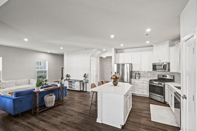 kitchen with appliances with stainless steel finishes, a kitchen island, white cabinetry, dark hardwood / wood-style flooring, and a breakfast bar