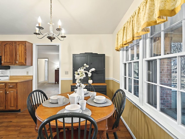 dining space with dark hardwood / wood-style flooring, a notable chandelier, and wooden walls