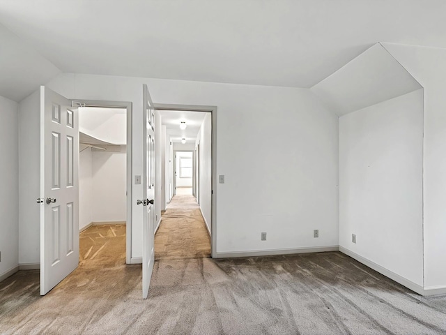 unfurnished bedroom with a walk in closet, vaulted ceiling, carpet, and a closet