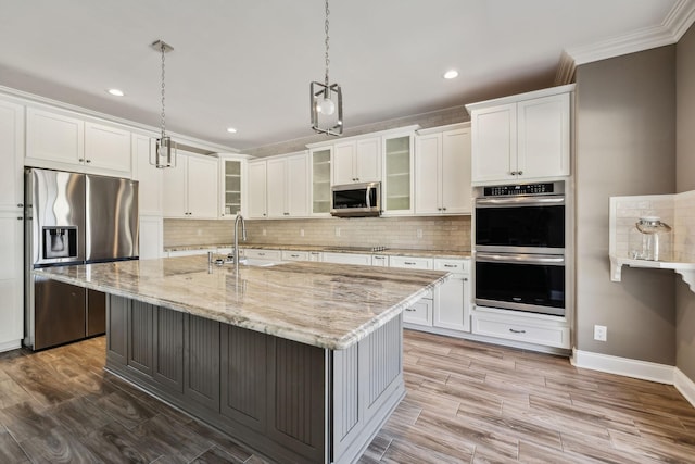 kitchen featuring stainless steel appliances, an island with sink, sink, hanging light fixtures, and light stone counters