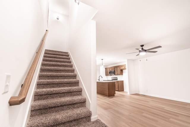 staircase with ceiling fan, wood finished floors, and baseboards