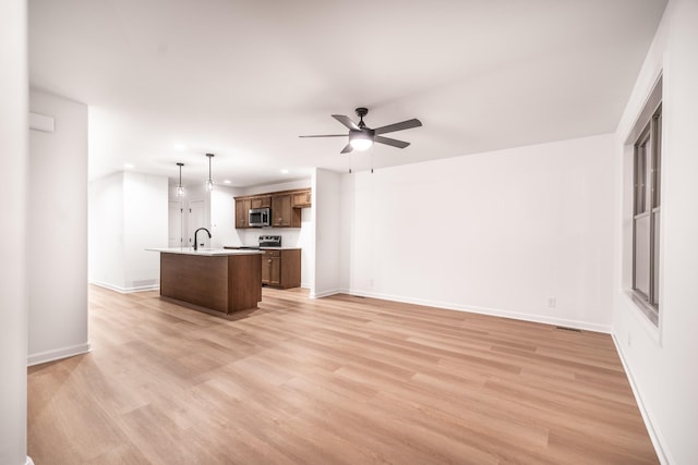 kitchen featuring a ceiling fan, light countertops, appliances with stainless steel finishes, light wood-type flooring, and an island with sink