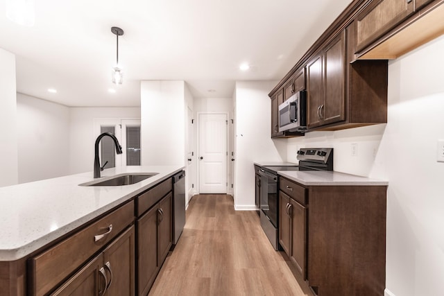 kitchen featuring dark brown cabinetry, light wood-style flooring, light stone countertops, stainless steel appliances, and a sink