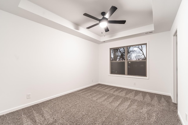 spare room with a tray ceiling, dark carpet, visible vents, and baseboards