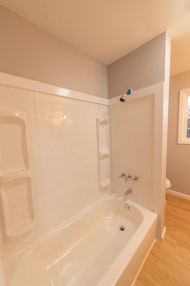 bathroom with hardwood / wood-style flooring, shower / bathing tub combination, and toilet