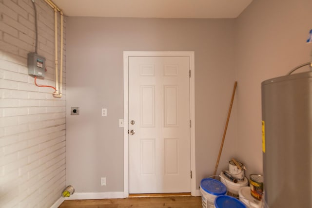 washroom with hardwood / wood-style flooring, brick wall, electric dryer hookup, and water heater