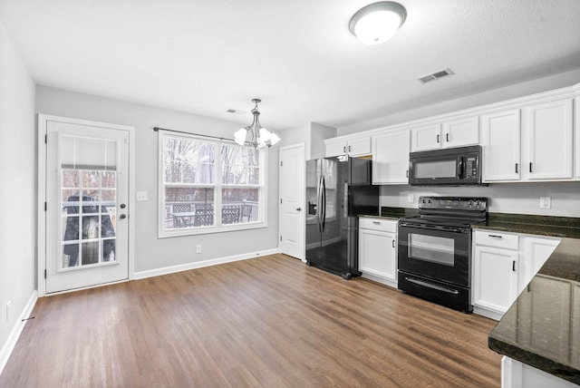 kitchen featuring dark wood-type flooring, white cabinetry, hanging light fixtures, dark stone countertops, and black appliances