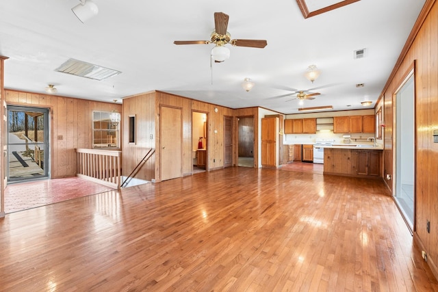 unfurnished living room featuring ceiling fan, wood walls, and light wood-type flooring