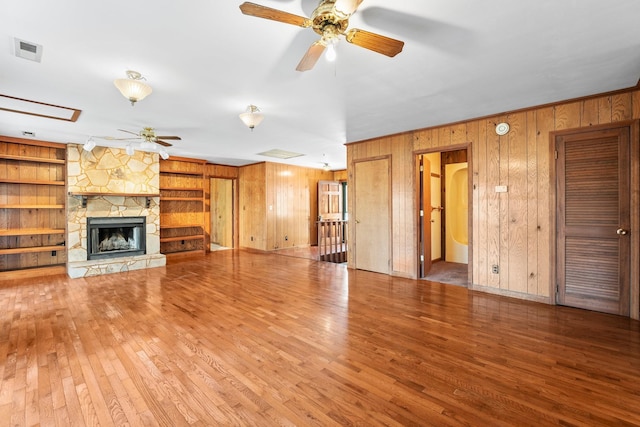 unfurnished living room with built in shelves, wood walls, hardwood / wood-style flooring, ceiling fan, and a fireplace