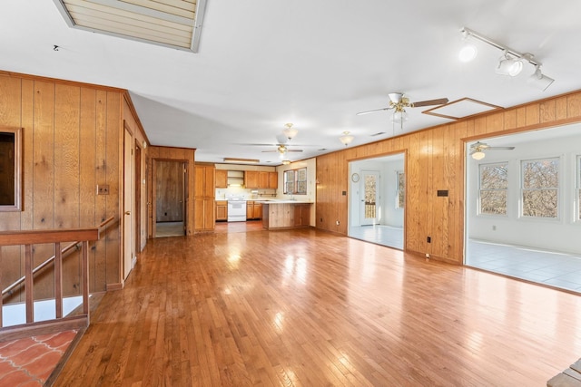 unfurnished living room featuring light hardwood / wood-style flooring, ceiling fan, and wood walls