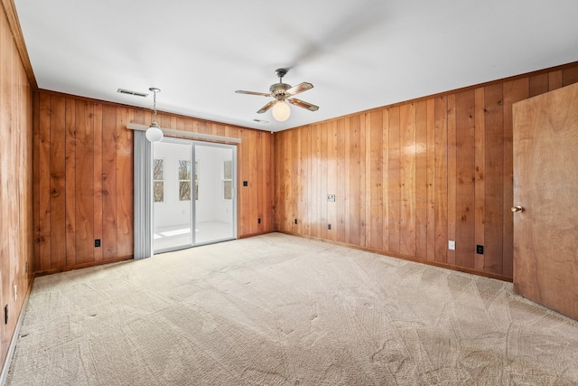 unfurnished room featuring light colored carpet, ceiling fan, and wood walls