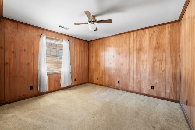 carpeted empty room with crown molding, wooden walls, and ceiling fan