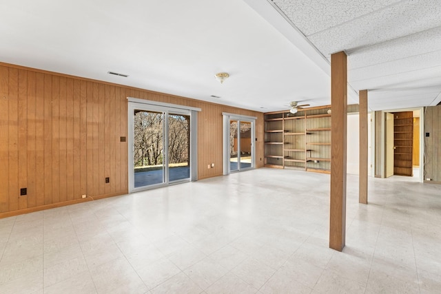 unfurnished living room with ceiling fan and wooden walls